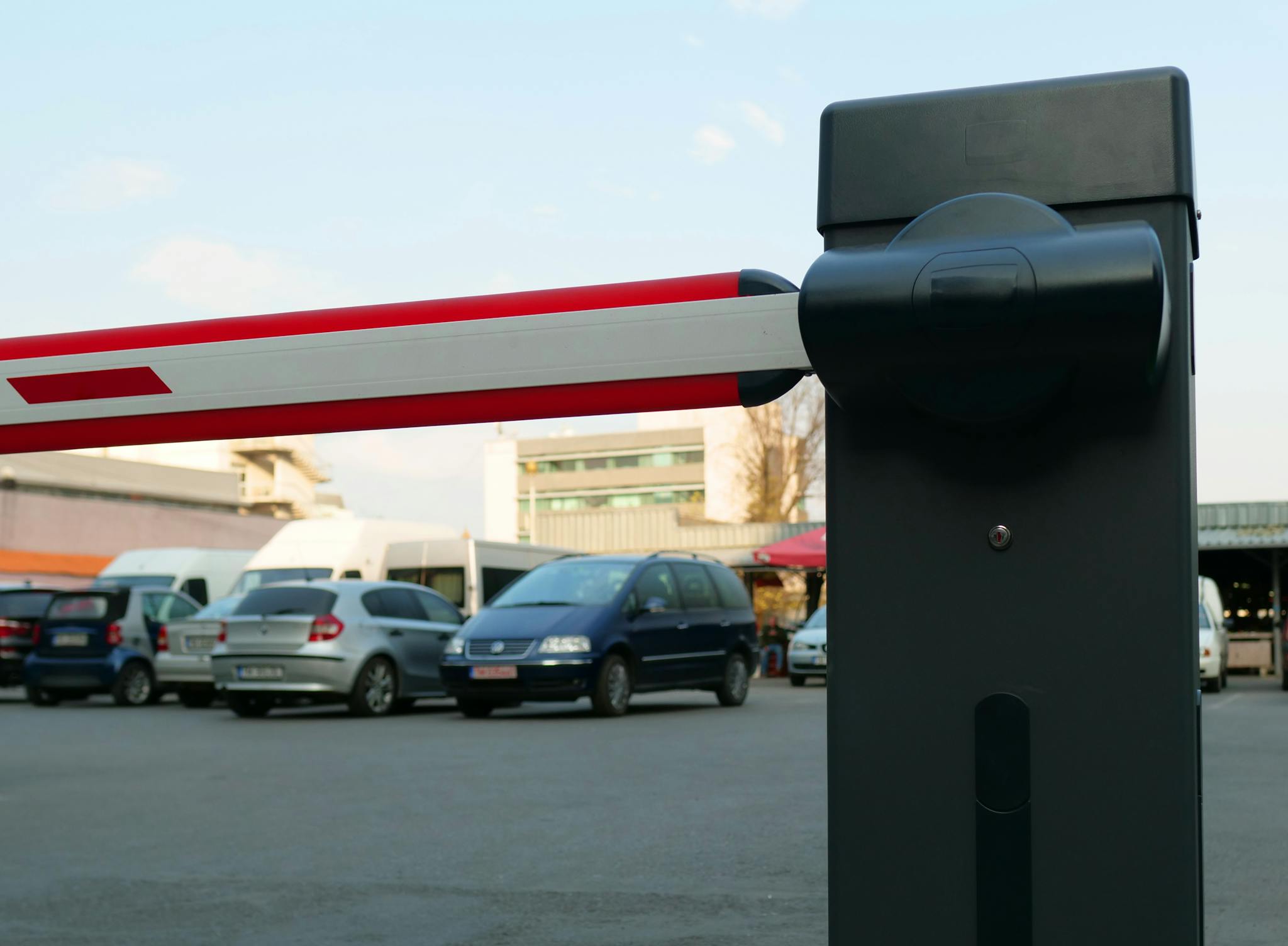 Close-up of a parking lot barrier gate with vehicles in the background, modern and automated.